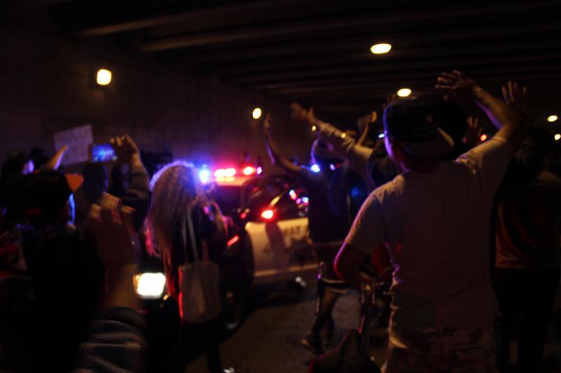 Protesters surround a cop car under the 110 Freeway. (Rebecca Gibian/Neon Tommy)