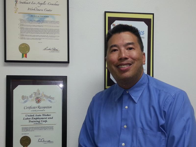 Bryant Eng poses in front of various awards at the South L.A. WorkSource Center, Dec. 8, 2014. (Taylor Haney/Neon Tommy)