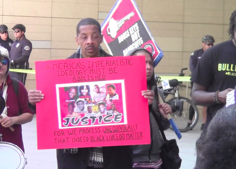 A protestor showing the faces of black people who have died at the hands of the police. (Taylor Villanueva/Neon Tommy)