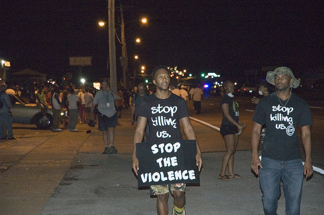 Ten days after the shooting of Michael Brown on Aug. 9, protesters in Ferguson, Missouri rallied on the streets wearing shirts that state, "Stop killing us." (peoplesworld/Creative Commons)