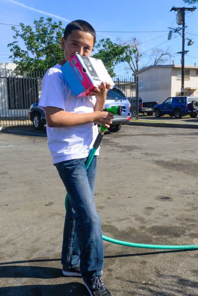 Edgar Jaime, 12, holding a hose and a donation box in the Jordan Downs housing project Saturday afternoon in Watts. Edgar was helping at a car wash to raise money for a neighbor, whose mother recently passed away. (Charlie Magovern/Neon Tommy)
